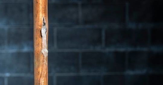 Ruptured copper water supply line covered in frost and ice against a basement wall